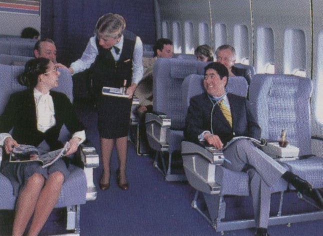 1980s A flight attendant assiting a customer in an early version of the Clipper Class (business class) cabin  with 8 across seating.